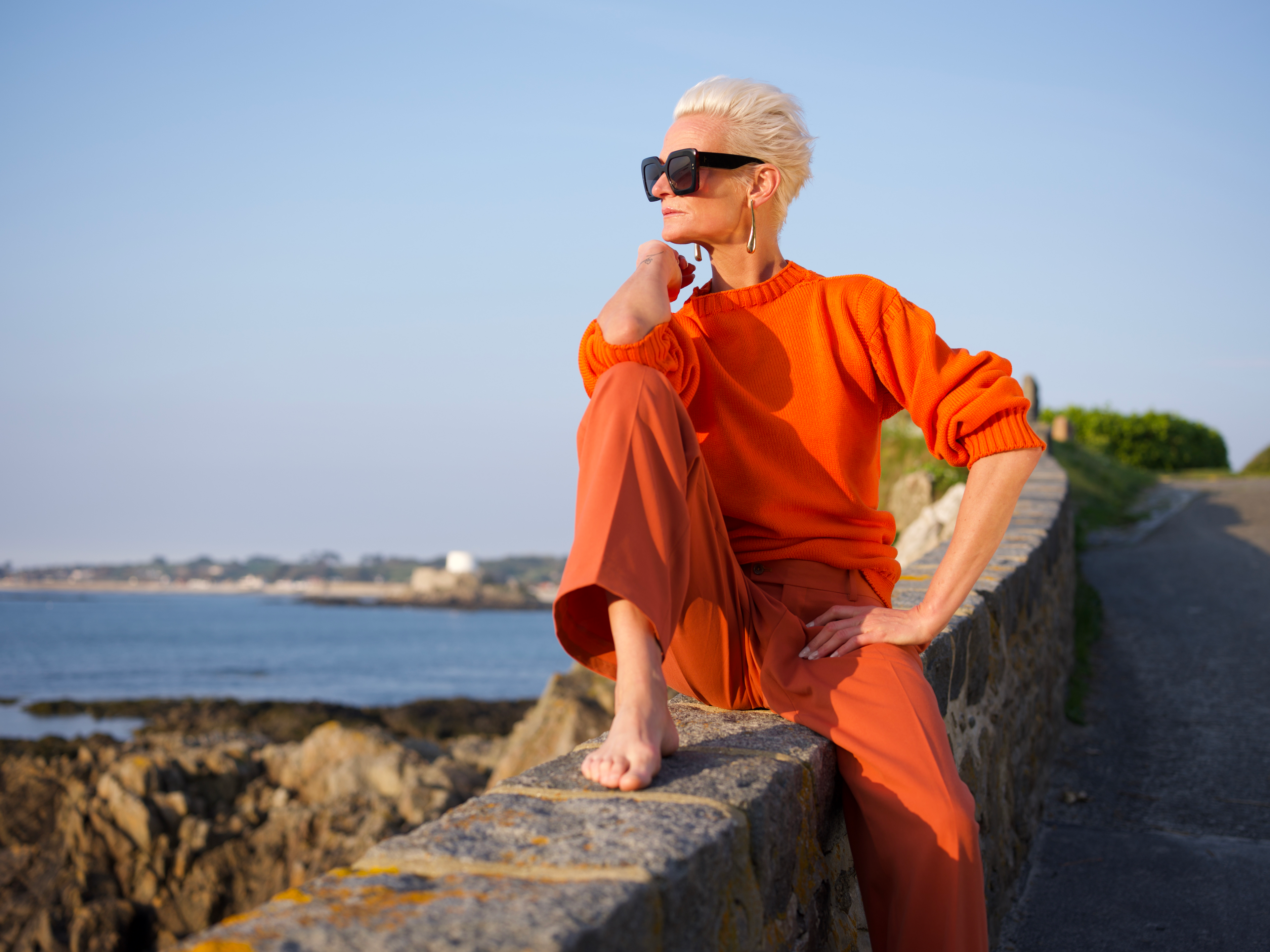 Woman in a LYNNE orange cashmere Guernsey by the sea.
